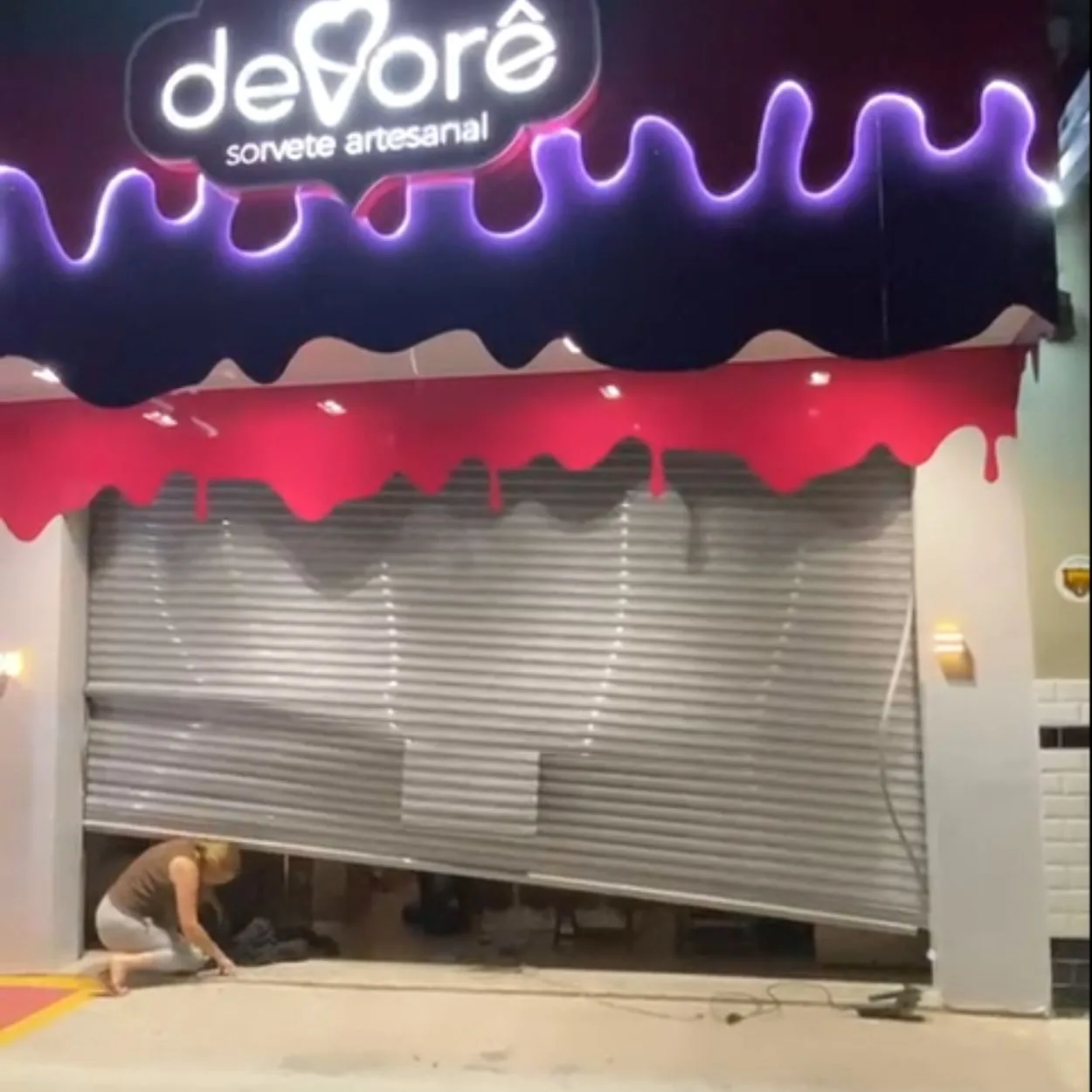 Porta de aço danificada em fachada de loja antes do conserto emergencial