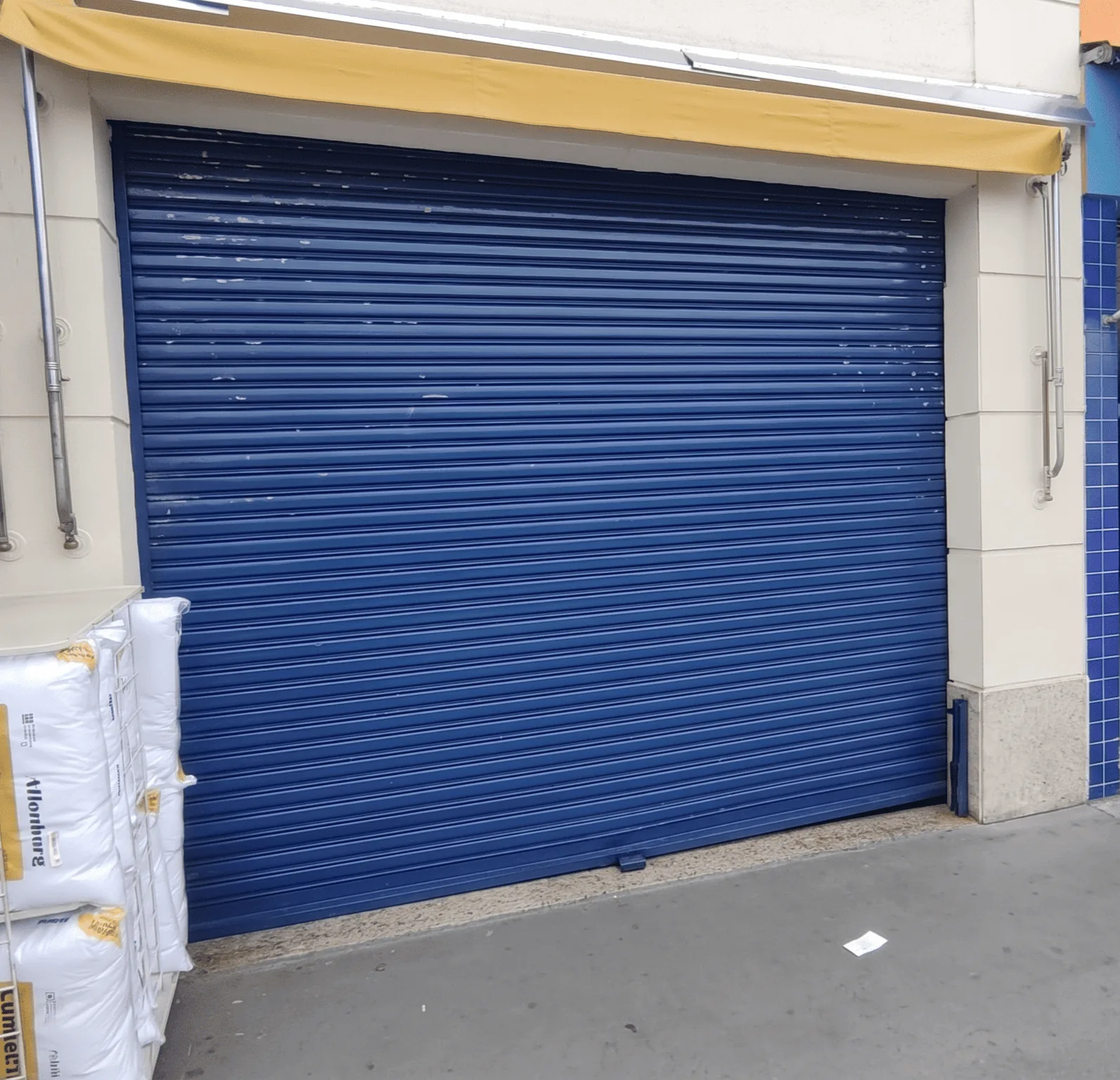 Porta de aço de enrolar com pintura azul instalada em fachada de comércio